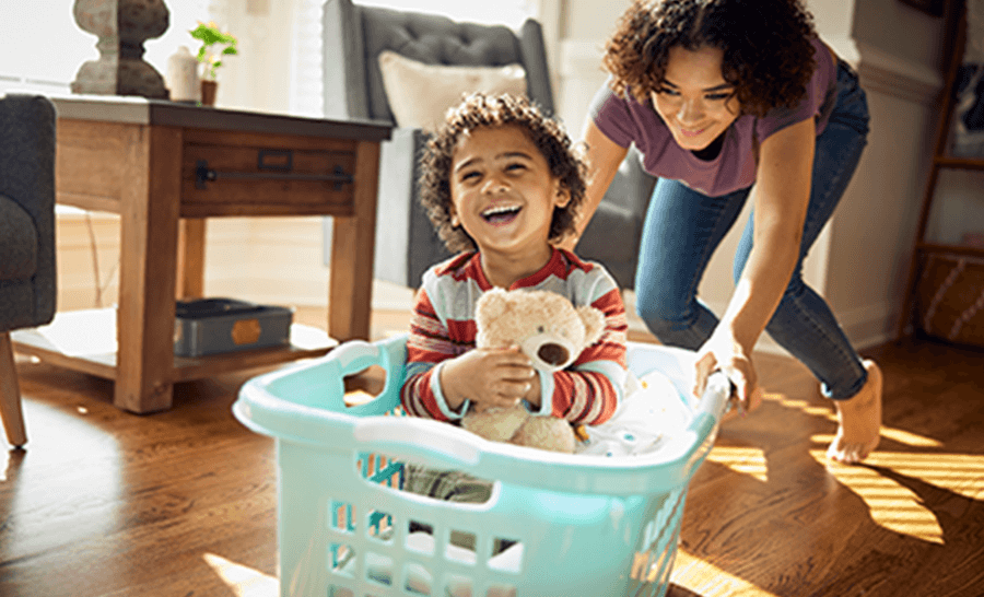 Care free moment of sister pushing younger sibling in a laundry basket pretending it’s a car 